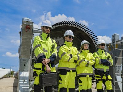 A team of engineers stands in front of large wind turbine components at a construction site, ready for installation. The scene highlights teamwork, renewable energy, and wind power technology.