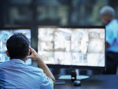 Security guard in control room, man checking cctv screen in surveillance office for building safety.